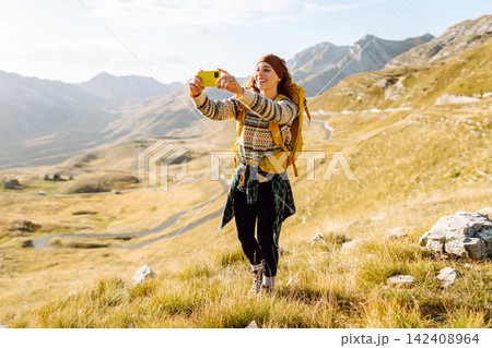 A young woman captures a moment while hiking in a mountainous landscape during golden hour A young woman captures a moment while hiking in a mountainous landscape during golden hour 142408964
