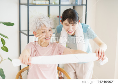 タオルを持って体操をするシニア日本人女性と若い日本人介護士 142409021