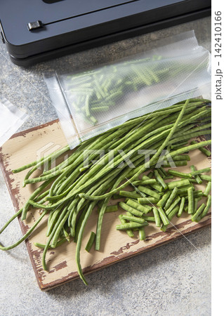 Vacuum sealed fresh green beans in packaging and vacuum sealer on a light grey background, healthy eating, zero waste, meal prep concept. Vacuum sealed fresh green beans in packaging and vacuum sealer on a light grey background, healthy eating, zero waste, meal prep concept. 142410166