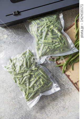 Vacuum sealed fresh green beans in packaging and vacuum sealer on a light grey background, healthy eating, zero waste, meal prep concept. Top view flat lay background. Vacuum sealed fresh green beans in packaging and vacuum sealer on a light grey background, healthy eating, zero waste, meal prep concept. Top view flat lay background. 142410171