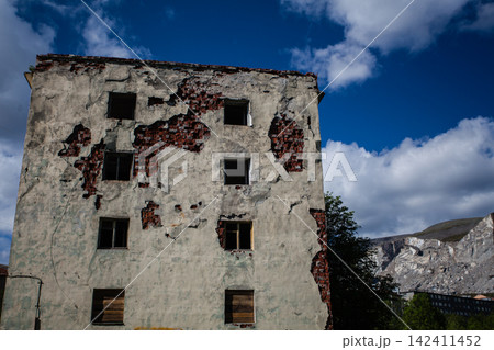 Decaying facade of an abandoned Soviet-era residential building in Kukisvumchorr, Kirovsk, Murmansk Region, Russia. Exposed red brickwork, crumbling plaster, broken windows and boarded openings show t Decaying facade of an abandoned Soviet-era residential building in Kukisvumchorr, Kirovsk, Murmansk Region, Russia. Exposed red brickwork, crumbling plaster, broken windows and boarded openings show t 142411452