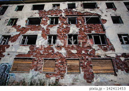 Decaying facade of an abandoned Soviet-era residential building in Kukisvumchorr, Kirovsk, Murmansk Region, Russia. Exposed red brickwork, crumbling plaster, broken windows and boarded openings show t Decaying facade of an abandoned Soviet-era residential building in Kukisvumchorr, Kirovsk, Murmansk Region, Russia. Exposed red brickwork, crumbling plaster, broken windows and boarded openings show t 142411453