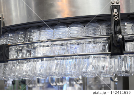 Overhead conveyor belt handling plastic bottles to filling process in drinking water factory Overhead conveyor belt handling plastic bottles to filling process in drinking water factory 142411659