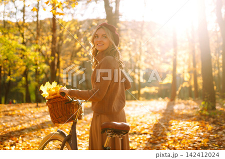 Stylish woman with a bicycle enjoying autumn weather in the park. Beautiful Woman in the autumn forest. Stylish woman with a bicycle enjoying autumn weather in the park. Beautiful Woman in the autumn forest. 142412024