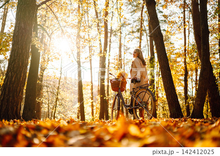 Stylish woman with a bicycle enjoying autumn weather in the park. Beautiful Woman in the autumn forest. Stylish woman with a bicycle enjoying autumn weather in the park. Beautiful Woman in the autumn forest. 142412025
