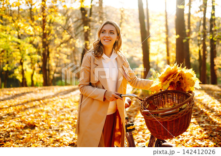Stylish woman with a bicycle enjoying autumn weather in the park. Beautiful Woman in the autumn forest. Stylish woman with a bicycle enjoying autumn weather in the park. Beautiful Woman in the autumn forest. 142412026