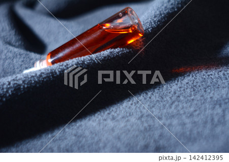 Horizontal view of a glass bottle with red liquid on blue textured fabric 142412395