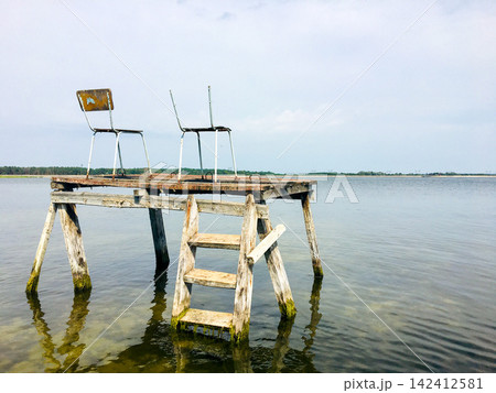 Rustic wooden diving dock with chairs in clear lake water 142412581