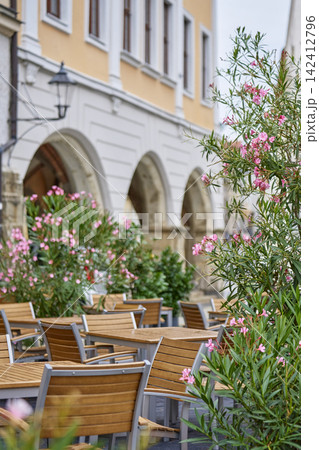 Empty outdoor cafe terrace with wooden tables and chairs surrounded by flowering plants Empty outdoor cafe terrace with wooden tables and chairs surrounded by flowering plants 142412796