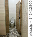 Opened wooden door reveals clean ceramic toilet bowl inside public restroom stall decorated with vintage patterned floor tiles, presenting hygienic sanitary facility 142412800