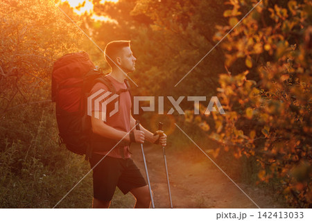 Hiker in forest with backpack and poles at sunset. Active lifestyle and adventure hiking 142413033
