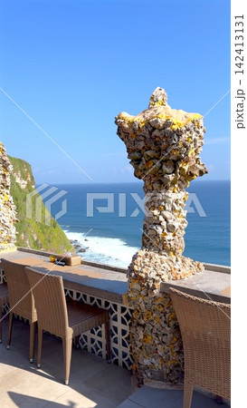 Clifftop terrace seating with woven chairs and textured coral column overlooking blue ocean, with ocean, cliff, terrace, seating detail, showing chair, rattan, table, reserved context 142413131