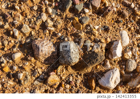 Detailed top-down view of a rustic sand and gravel quarry ground featuring textured natural stones, rocky debris, and gritty earth surface under bright daylight in a geological pit Detailed top-down view of a rustic sand and gravel quarry ground featuring textured natural stones, rocky debris, and gritty earth surface under bright daylight in a geological pit 142413355