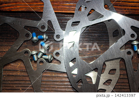 Close-up of polished steel bicycle disc brake rotors with blue threadlocker mounting bolts arranged on a dark rustic wooden background for professional bike maintenance and repair Close-up of polished steel bicycle disc brake rotors with blue threadlocker mounting bolts arranged on a dark rustic wooden background for professional bike maintenance and repair 142413397
