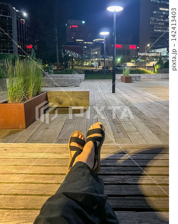 Person Relaxing on Wooden Bench at Night Waterfront Promenade Person Relaxing on Wooden Bench at Night Waterfront Promenade 142413403