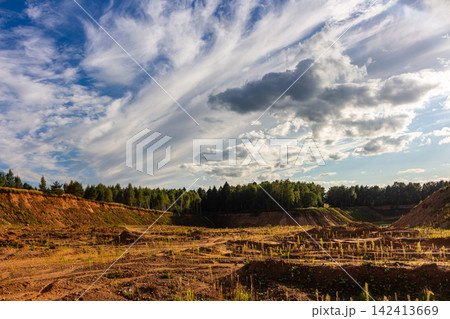 Vast sandy quarry with rugged textured ground and scattered greenery under a dramatic sky with wispy clouds, capturing the raw beauty of an industrial landscape at golden hour Vast sandy quarry with rugged textured ground and scattered greenery under a dramatic sky with wispy clouds, capturing the raw beauty of an industrial landscape at golden hour 142413669