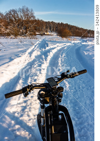 Electric fat bike POV shot on a crisp winter day, handlebars leading the way along a snowy path with fresh tracks through a serene frosty landscape Electric fat bike POV shot on a crisp winter day, handlebars leading the way along a snowy path with fresh tracks through a serene frosty landscape 142413809