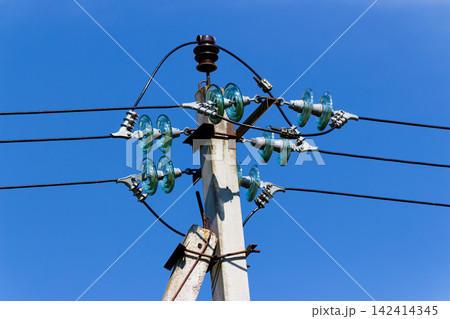 Concrete utility pole with glass insulators holding electrical power lines against a clear blue sky, showing industrial equipment for energy distribution and high voltage grid infrastructure 142414345