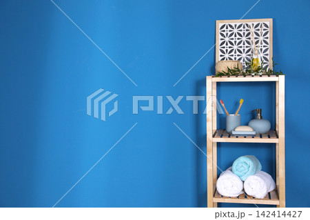 Shelving unit with toiletries near blue wall indoors, space for text. Bathroom interior element Shelving unit with toiletries near blue wall indoors, space for text. Bathroom interior element 142414427