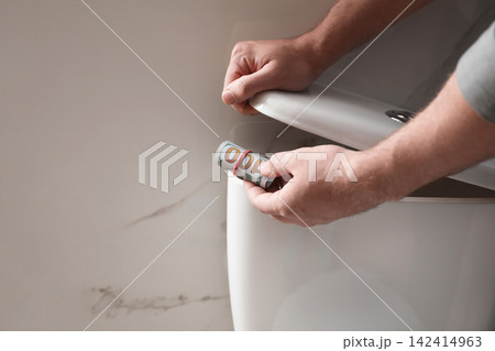 Man hiding money in toilet tank indoors, closeup. Financial savings Man hiding money in toilet tank indoors, closeup. Financial savings 142414963