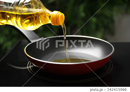 Pouring cooking oil from bottle into frying pan, closeup Pouring cooking oil from bottle into frying pan, closeup 142415066