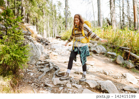 A person walks on a forest trail with a yellow backpack. Trees line both sides of the path. 142415199