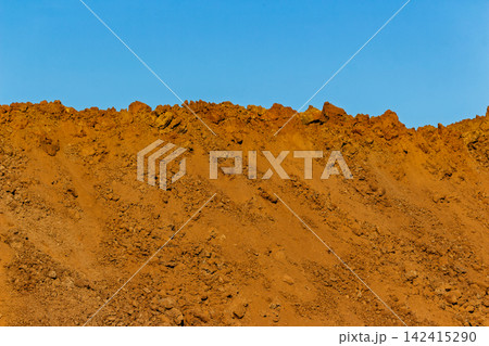 Large heaps of raw soil and dirt piled up at a construction site against a clear blue sky, textured mounds of earth showing excavation progress in bright daylight Large heaps of raw soil and dirt piled up at a construction site against a clear blue sky, textured mounds of earth showing excavation progress in bright daylight 142415290