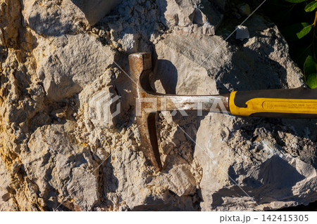 Close-up of a steel geological hammer resting on raw limestone rock at a quarry, used for expert fossil hunting and exploring mineral samples during outdoor fieldwork expeditions 142415305