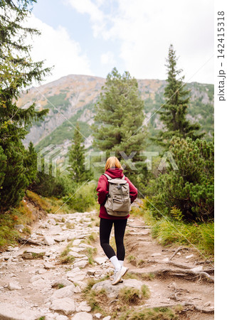 Woman hiking along a rocky trail surrounded by trees on a sunny day in the mountains 142415318