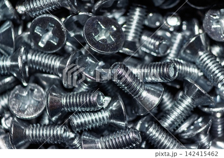 Close-up of numerous shiny galvanized countersunk head screws DIN 965. Dense metallic hardware background texture Close-up of numerous shiny galvanized countersunk head screws DIN 965. Dense metallic hardware background texture 142415462