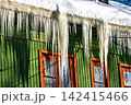 Bright winter sun illuminates sharp icicles adorning an old green wooden house, a visual reminder of cold days and potential heat loss from aging structures, Russia 142415466