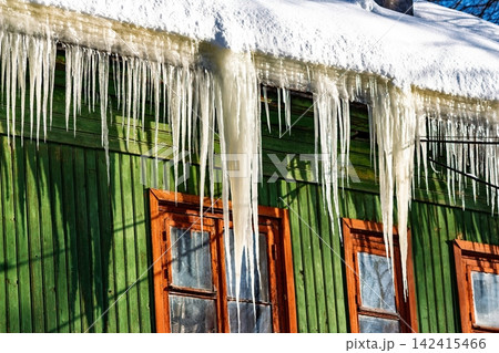 Bright winter sun illuminates sharp icicles adorning an old green wooden house, a visual reminder of cold days and potential heat loss from aging structures, Russia Bright winter sun illuminates sharp icicles adorning an old green wooden house, a visual reminder of cold days and potential heat loss from aging structures, Russia 142415466