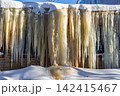 Massive frozen icicles cascade down a building facade, glistening in the cold morning light. An impressive urban winter wonderland scene 142415467