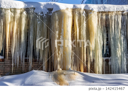 Massive frozen icicles cascade down a building facade, glistening in the cold morning light. An impressive urban winter wonderland scene Massive frozen icicles cascade down a building facade, glistening in the cold morning light. An impressive urban winter wonderland scene 142415467