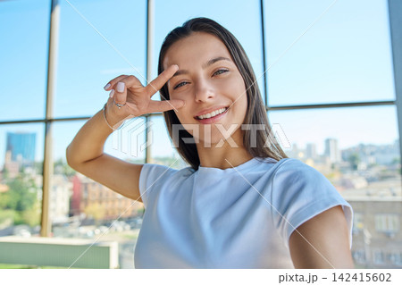 Young smiling woman holding victory sign near eye while taking selfie photo Young smiling woman holding victory sign near eye while taking selfie photo 142415602