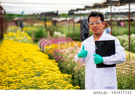 Researcher man giving thumbs up with clipboard in colorful flower nursery, confident positive expression representing science, horticulture, plant quality, success and professional approval Researcher man giving thumbs up with clipboard in colorful flower nursery, confident positive expression representing science, horticulture, plant quality, success and professional approval 142417132