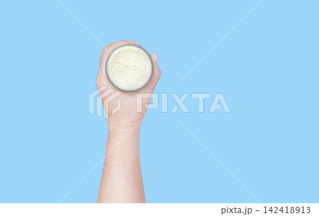 A hand holding a glass of milk against a blue background, top view. 142418913