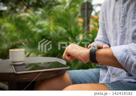 Freelancer using smartwatch and tablet at a tropical cafe 142419182