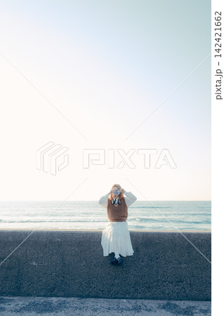 海を背景にフィルムカメラを構える若い女性 海を背景にフィルムカメラを構える若い女性 142421662
