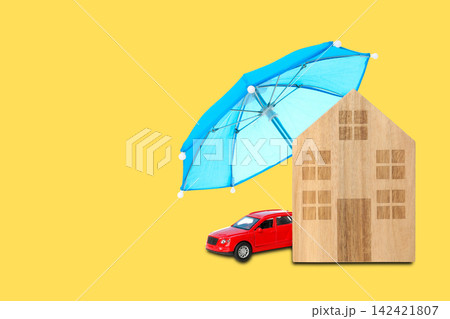 Insurance. Wooden house and red car placed under umbrella on yellow backdrop 142421807
