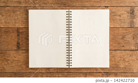 Open blank spiral notebook displaying empty white paper pages resting flat upon rustic brown wooden table surface viewed from directly above top down perspective Open blank spiral notebook displaying empty white paper pages resting flat upon rustic brown wooden table surface viewed from directly above top down perspective 142422710