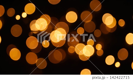 Blurry yellow golden circles randomly scattered across completely solid black background showing soft glowing out of focus light spots illuminating dark space 142422715