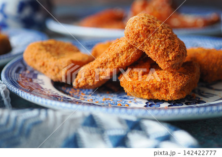 golden, crispy chicken nuggets served on a blue and white patterned plate 142422777