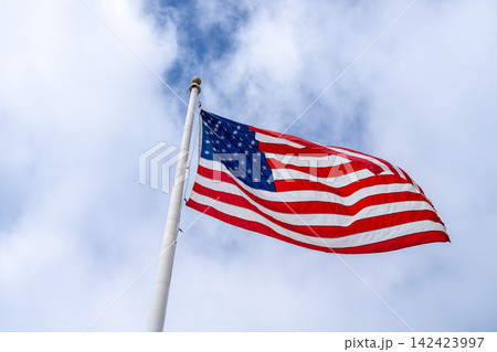 American flag waving on a tall pole against a cloudy sky 142423997