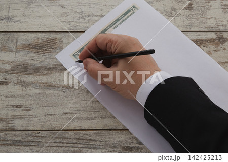 A businessman's hand draws a five-dollar bill with a pencil on a white piece of paper. A businessman's hand draws a five-dollar bill with a pencil on a white piece of paper. 142425213