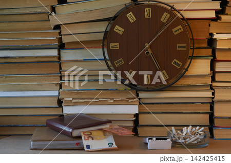 Large clock with Roman numerals on the clock face against a backdrop of stacked books, with organizers nearby from which euros are visible 142425415