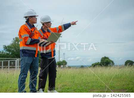 Two engineers inspecting wind turbine farm with laptop and walkie talkie. Two engineers inspecting wind turbine farm with laptop and walkie talkie. 142425565