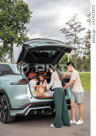 Asian family prepares their belongings while children sitting in a SUV trunk before going on a trip 142425655