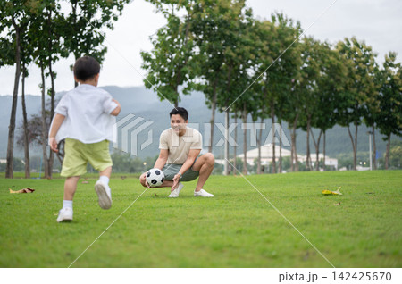Asian father and a young son playing soccer football together on a green grass field in the park. 142425670