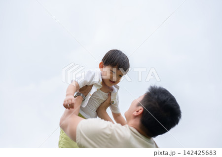 Asian father lifting his young kid son in the air with clear sky in background during joyful moment. 142425683